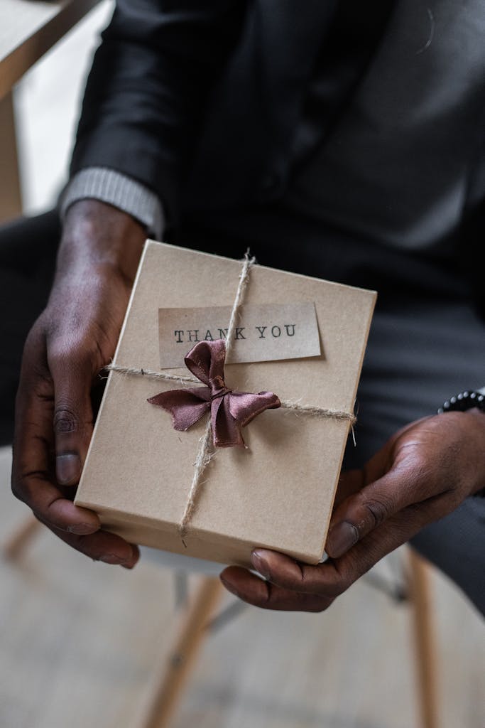 A close-up of a person holding a thank you gift wrapped with twine and a bow.
